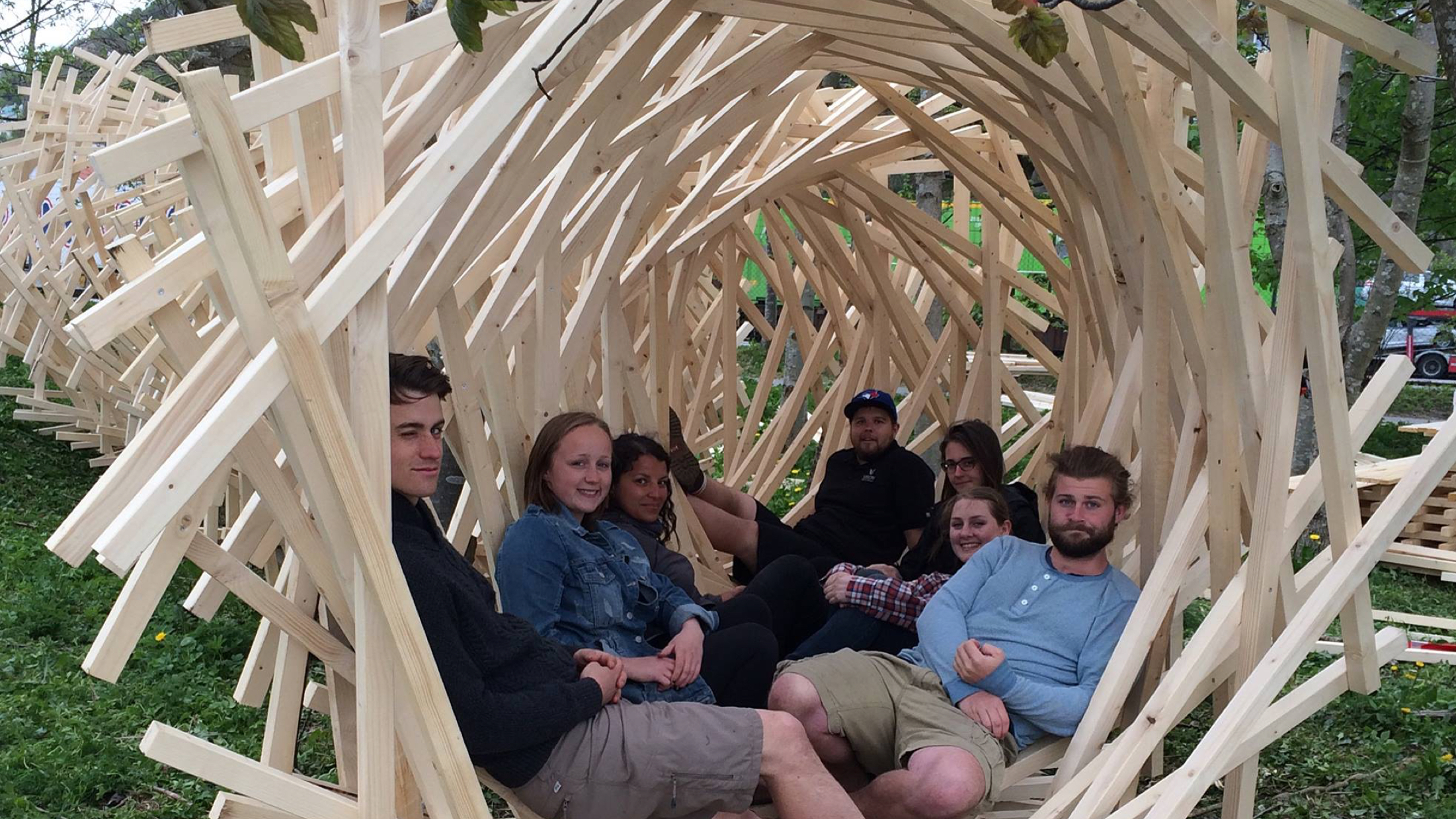 Photograph of a group of students sitting in a wooden arch structure they designed