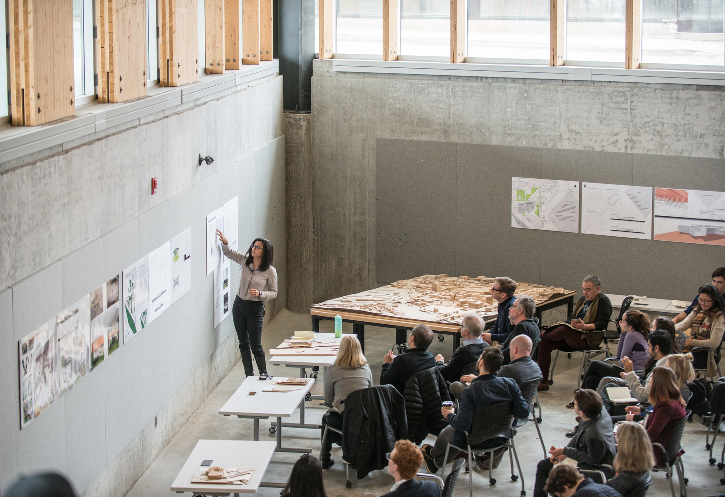 Photograph of a student presenting a poster to an audience in the McEwen School of Architecture's crit pit