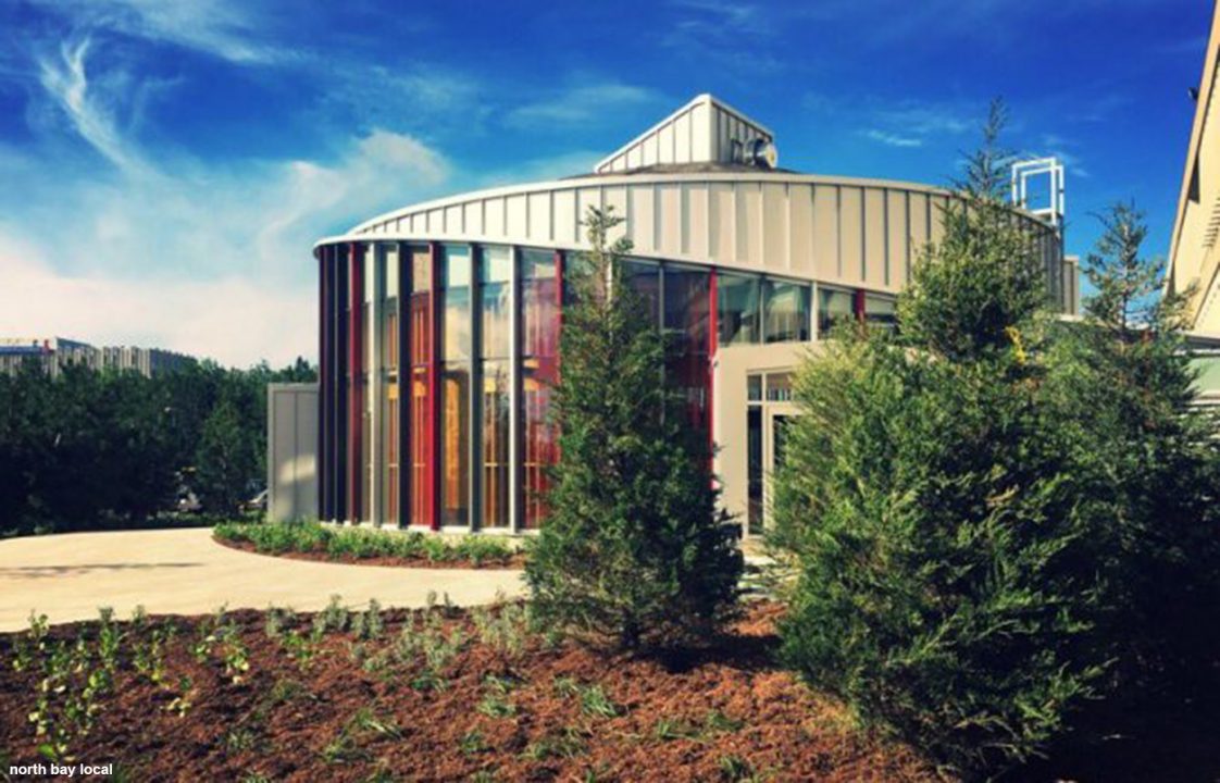 Photograph of a glass circular building with ever green trees in the front