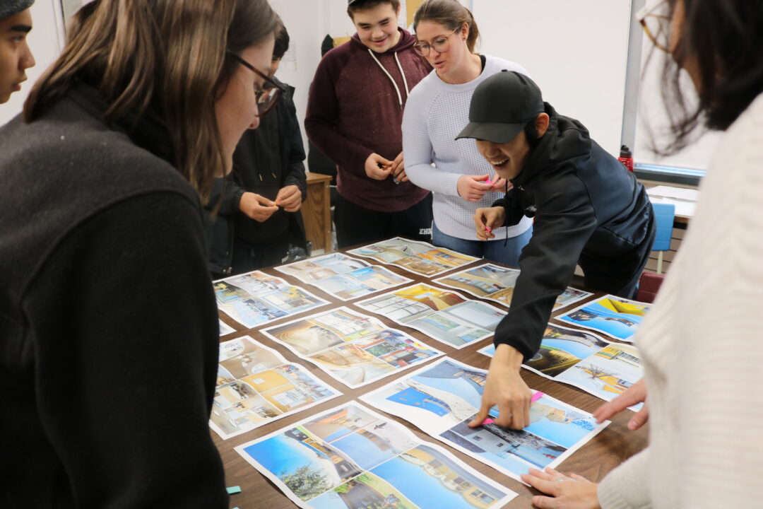 Photograph of students and community members speaking over a table with photographs