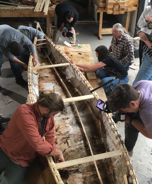 Photograph of students building a birch bark canoe with the help of an elder