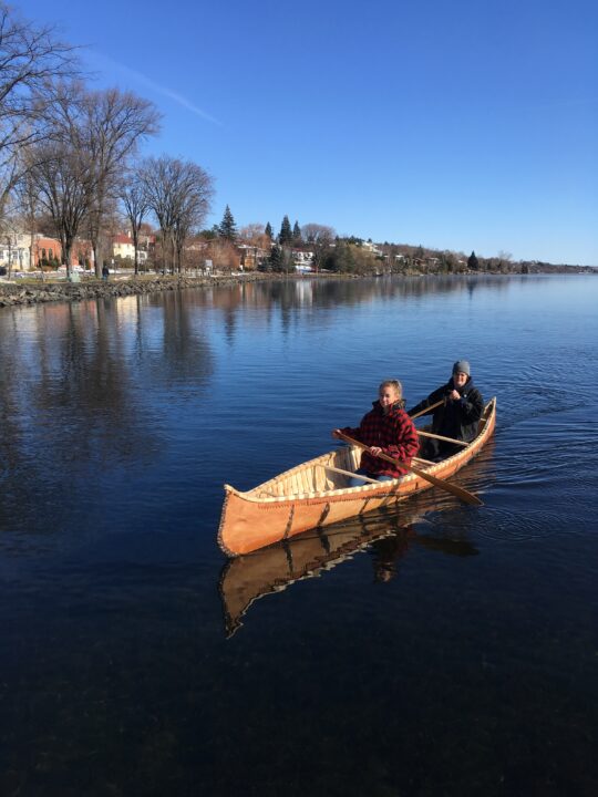 Photograph of two students canoeing in a birch bark canoe designed and built by the studio group