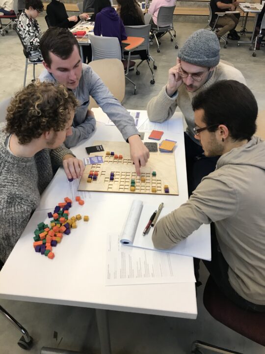 Photograph of students playing the board games they designed at multiple tables