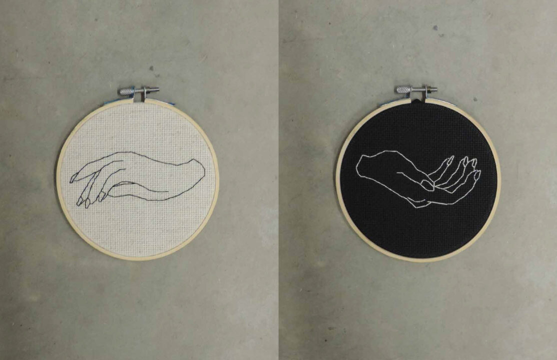 Photograph of two embroidery circles, one with a hand reaching down on a white background and the other with a hand reaching up on a black background