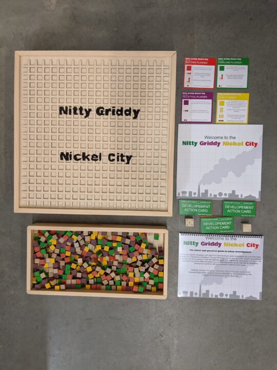 Photograph of a wooden grid board game with printed instructions and game pieces