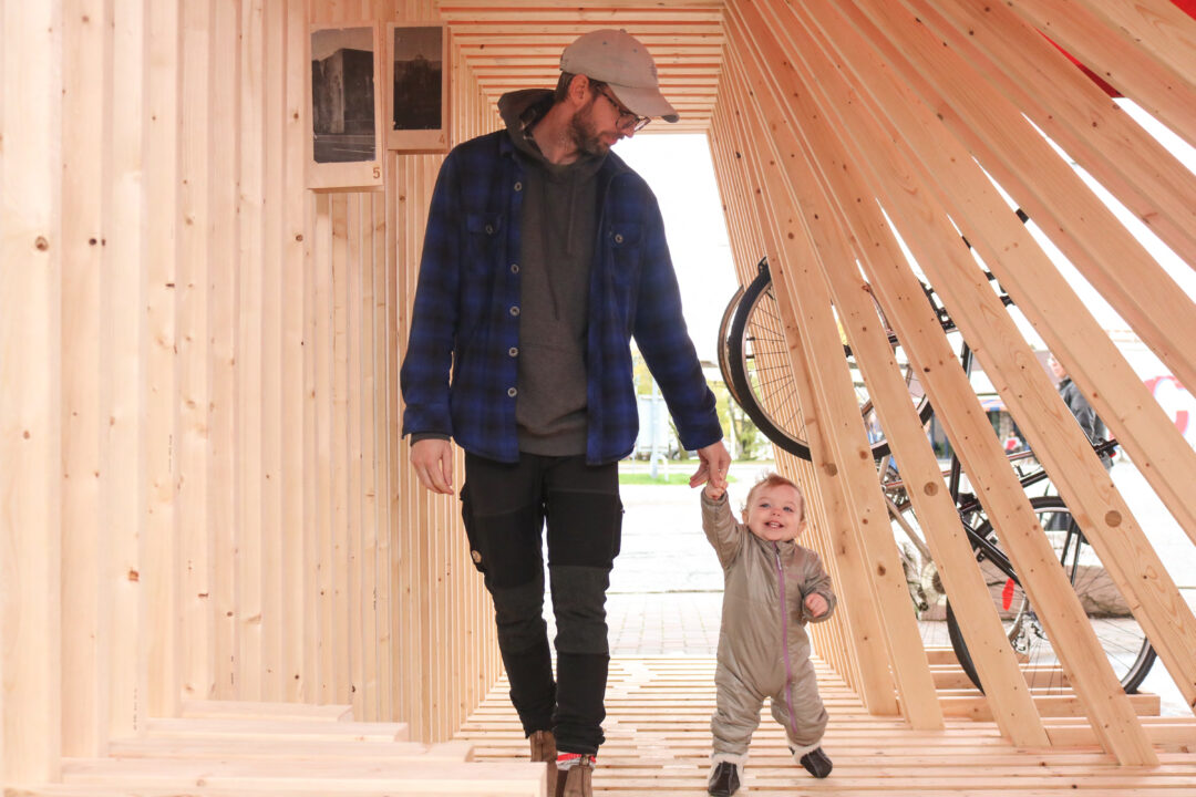 Photograph of a student and his child walking through a wooden student designed archway